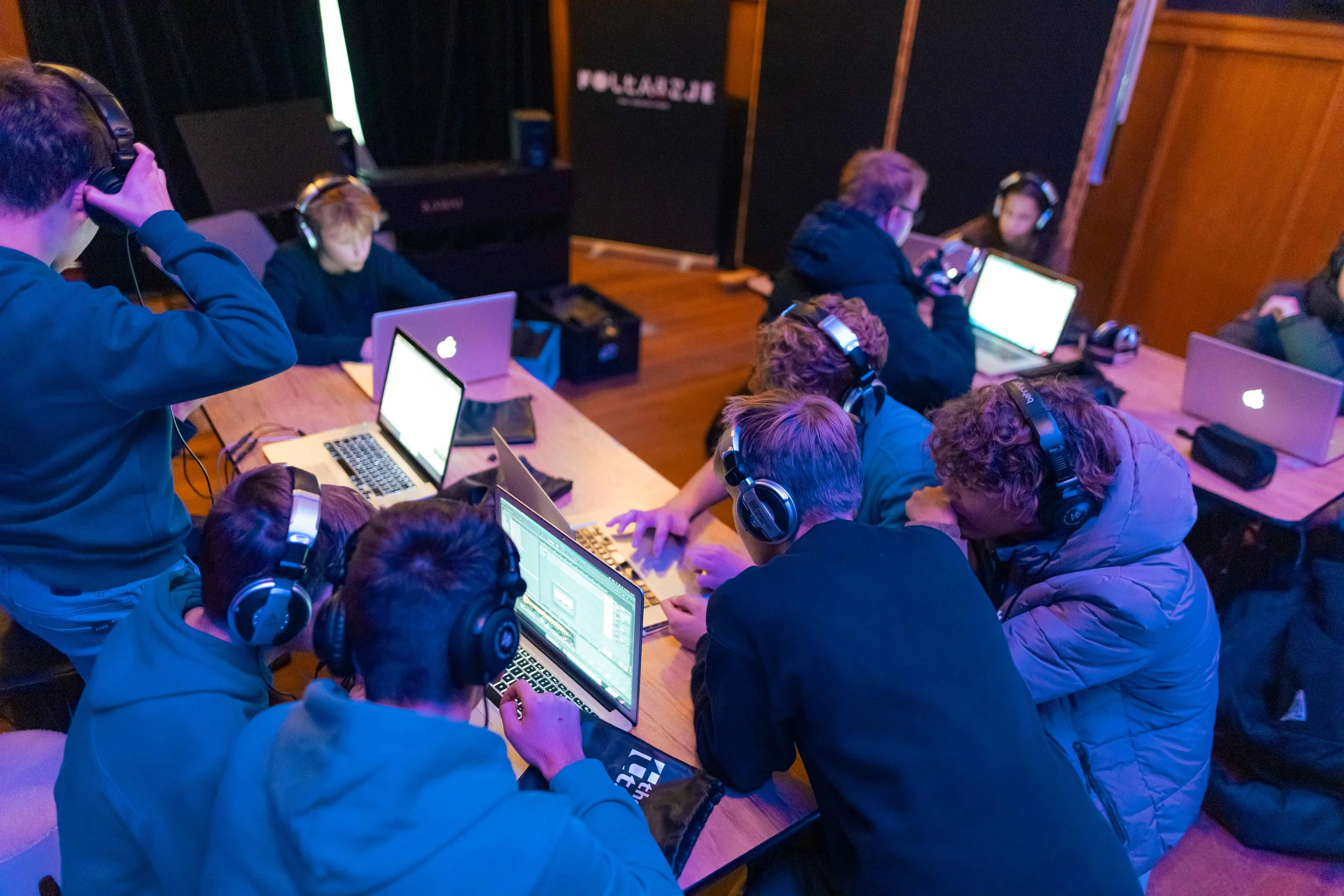 Group of young people wearing headphones working on laptops in a music or editing studio.
