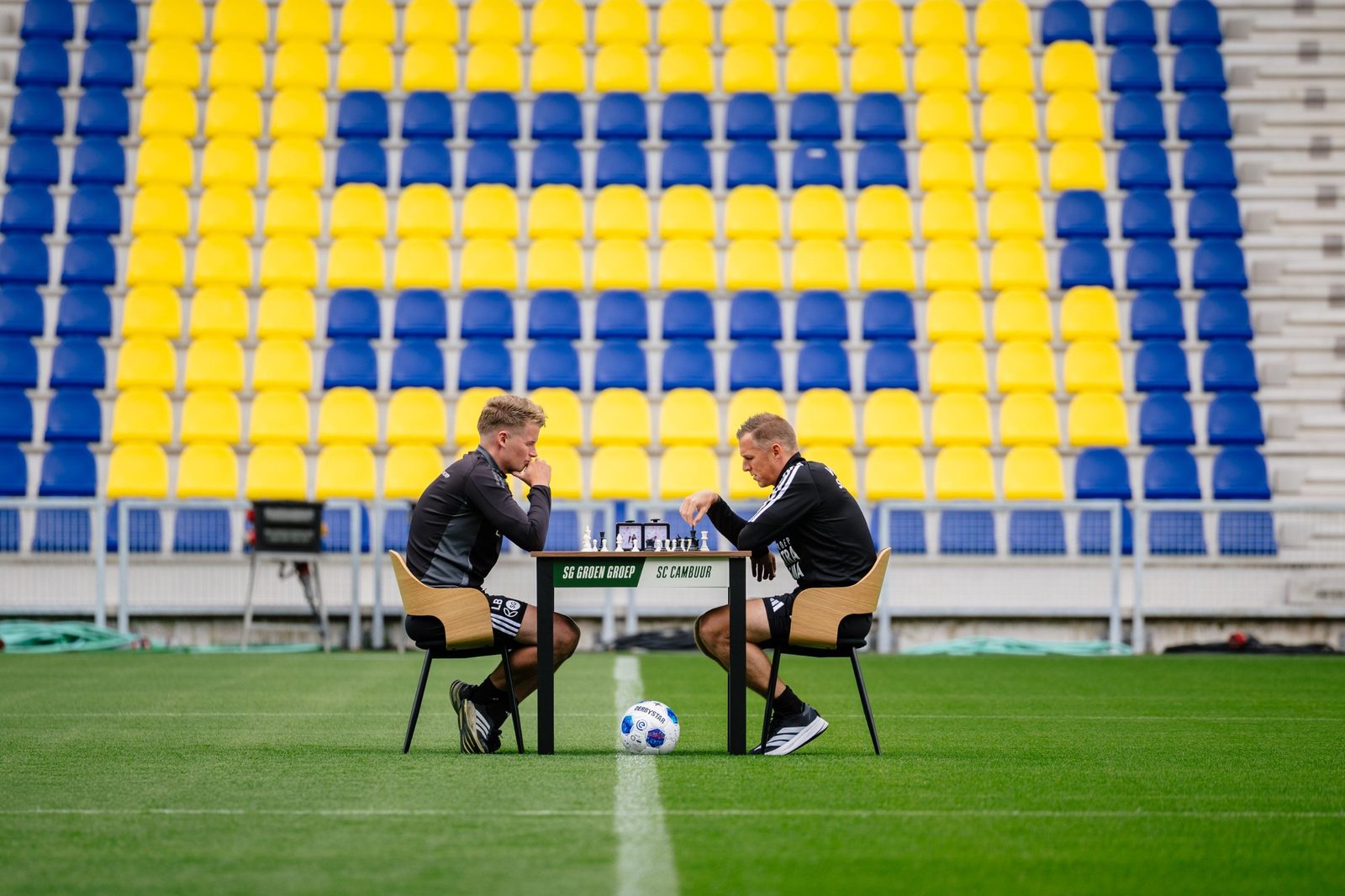 Twee spelers van SC Cambuur spelen schaak op het veld voor de geel-blauwe tribune